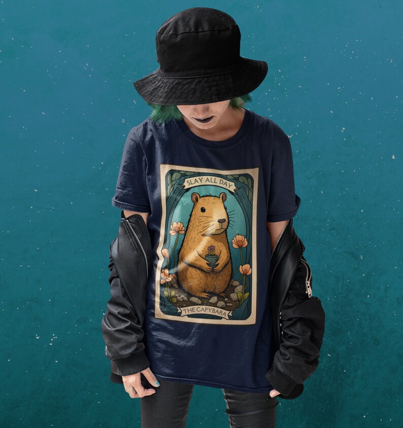 May include: A navy blue t-shirt with a graphic of a capybara holding a flower. The graphic is in a vintage style with the text "Slay All Day" and "The Capybara".