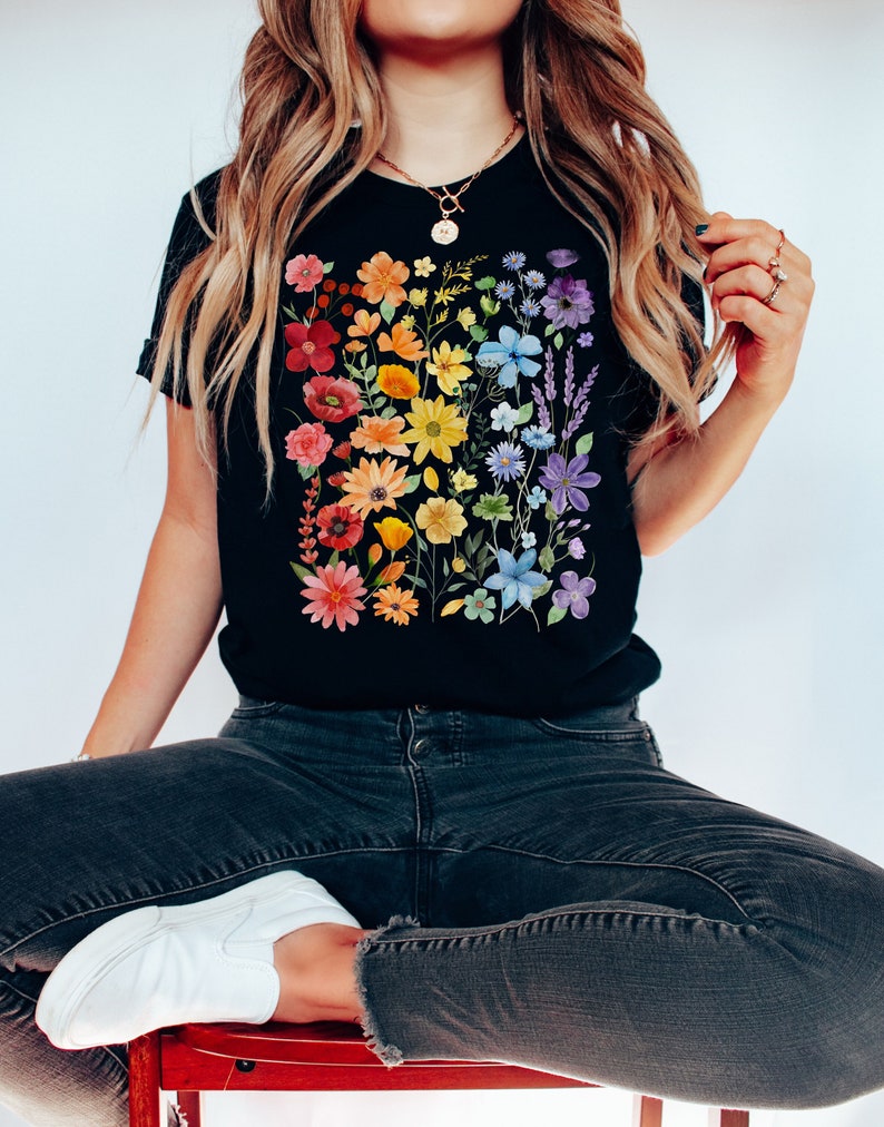 Puede incluir: Una camiseta negra con un estampado floral arco&iacute;ris. Las flores est&aacute;n dispuestas en una l&iacute;nea vertical y son de tonos rojos, naranjas, amarillos, verdes, azules y morados.