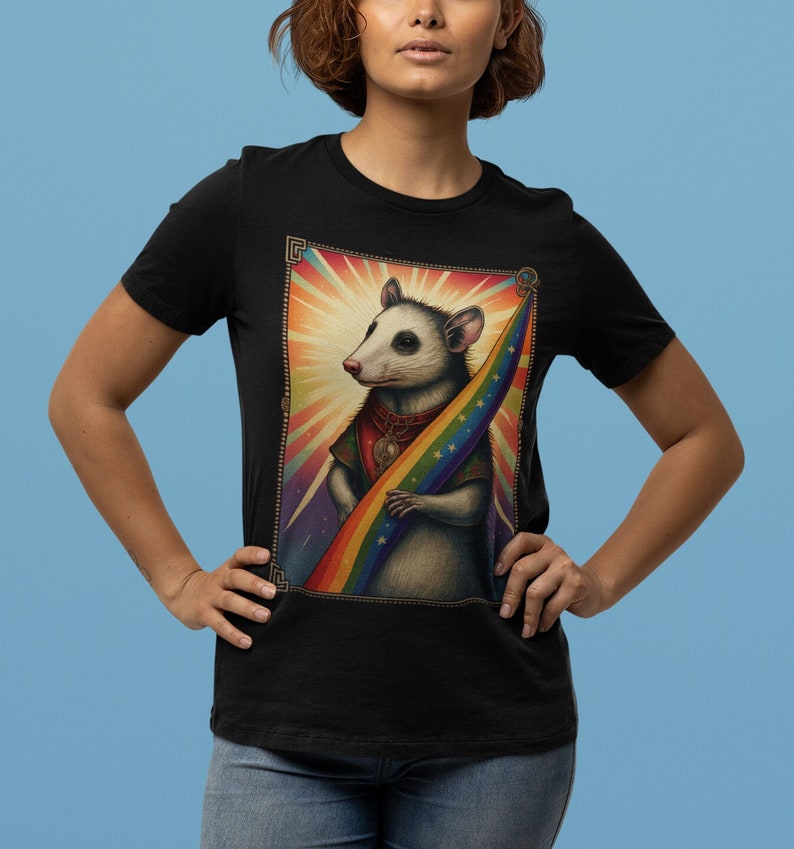 Pode incluir: Uma camiseta preta com um gr&aacute;fico de um gamb&aacute; segurando uma bandeira arco-&iacute;ris. O gamb&aacute; est&aacute; usando um colar de ouro com um pingente. O gr&aacute;fico &eacute; cercado por uma moldura dourada.