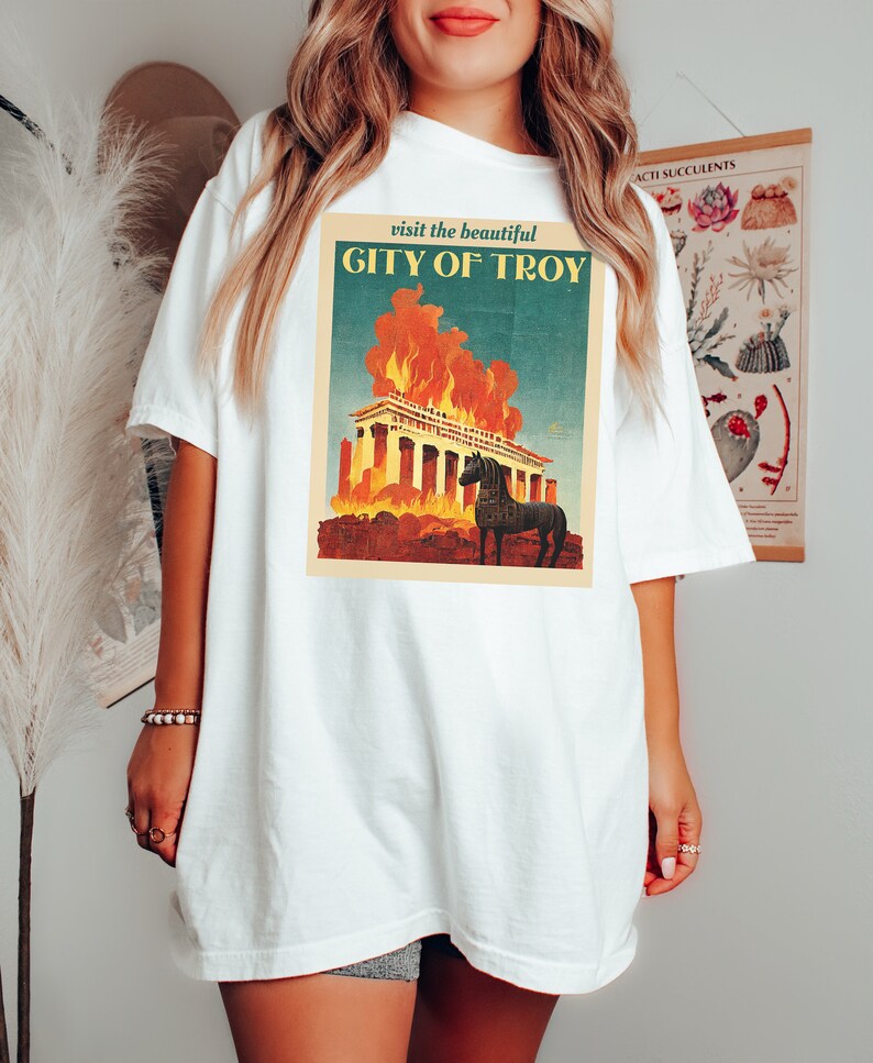 May include: White t-shirt with a vintage-style graphic of a burning building and a horse. The graphic says "visit the beautiful CITY OF TROY".