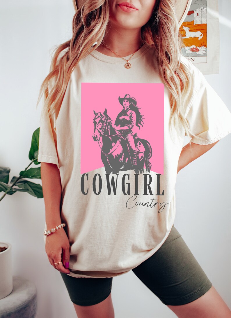 May include: A white t-shirt with a pink square featuring a silhouette of a cowgirl riding a horse. The text "COWGIRL Country" is printed below the image.