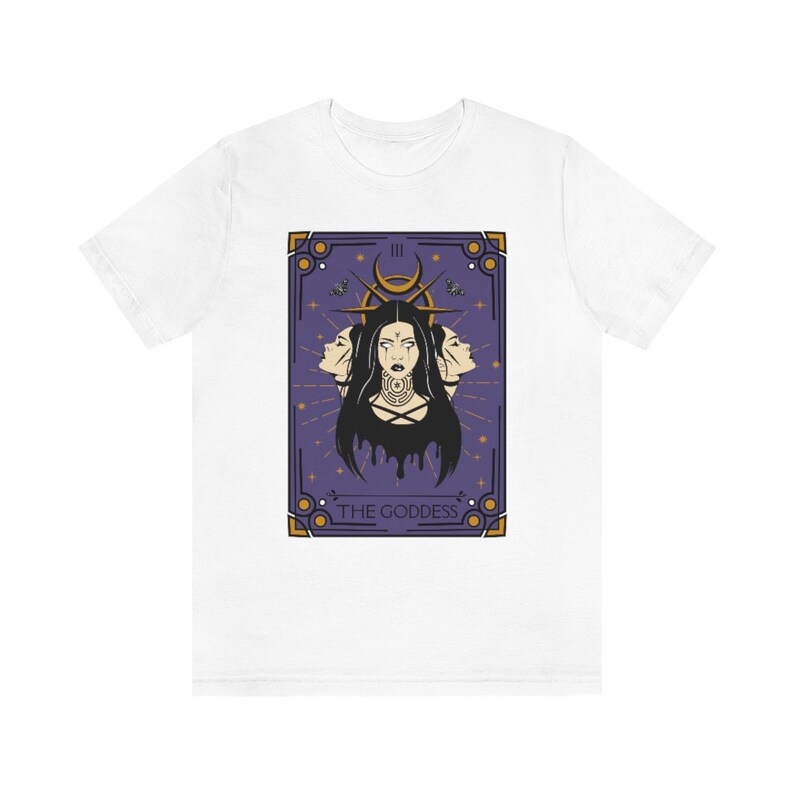 May include: White t-shirt with a purple and gold tarot card design. The card depicts a woman with three faces and the text "THE GODDESS" at the bottom.