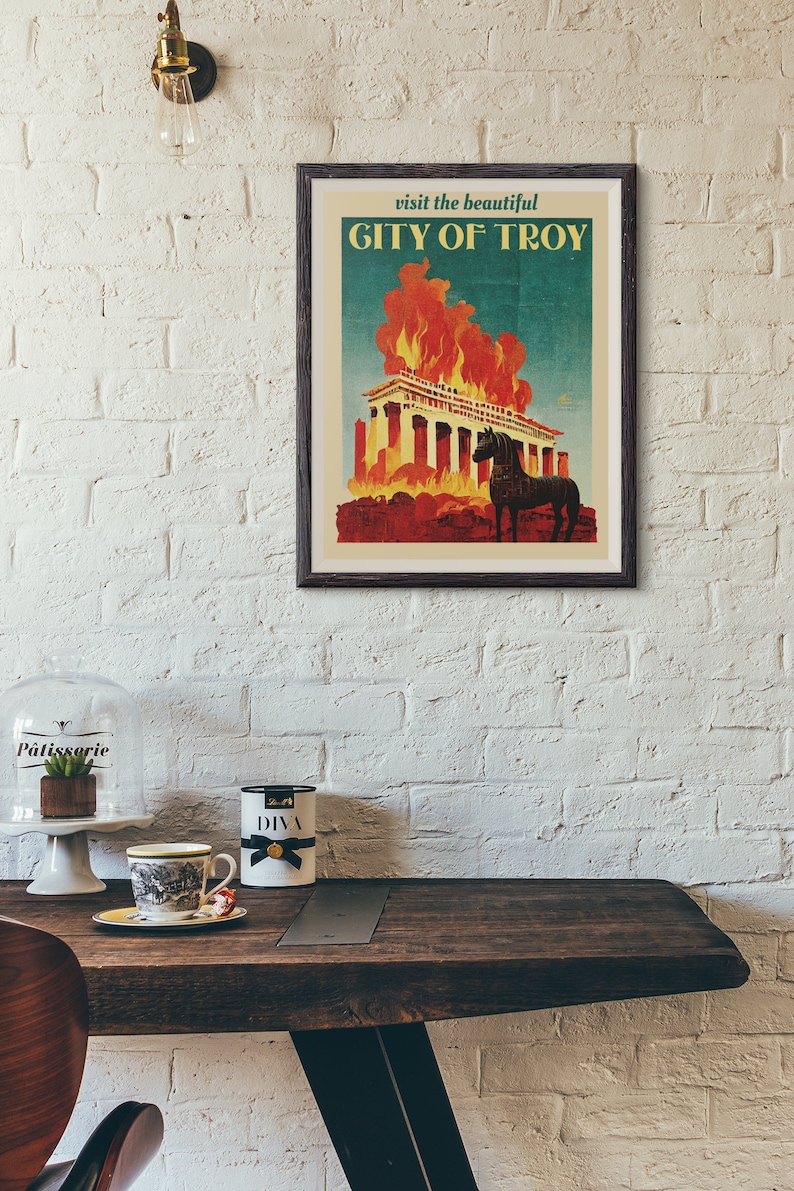 May include: A vintage travel poster with a dark wood frame. The poster features a blue background with the text "visit the beautiful CITY OF TROY" in white. The poster depicts a burning building with a black horse standing in front of it.