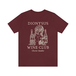May include: A maroon t-shirt with a white graphic of a bust of Dionysus, the Greek god of wine, with grapes and bottles of wine. The text "Dionysus Wine Club Charter Member" is printed below the graphic.