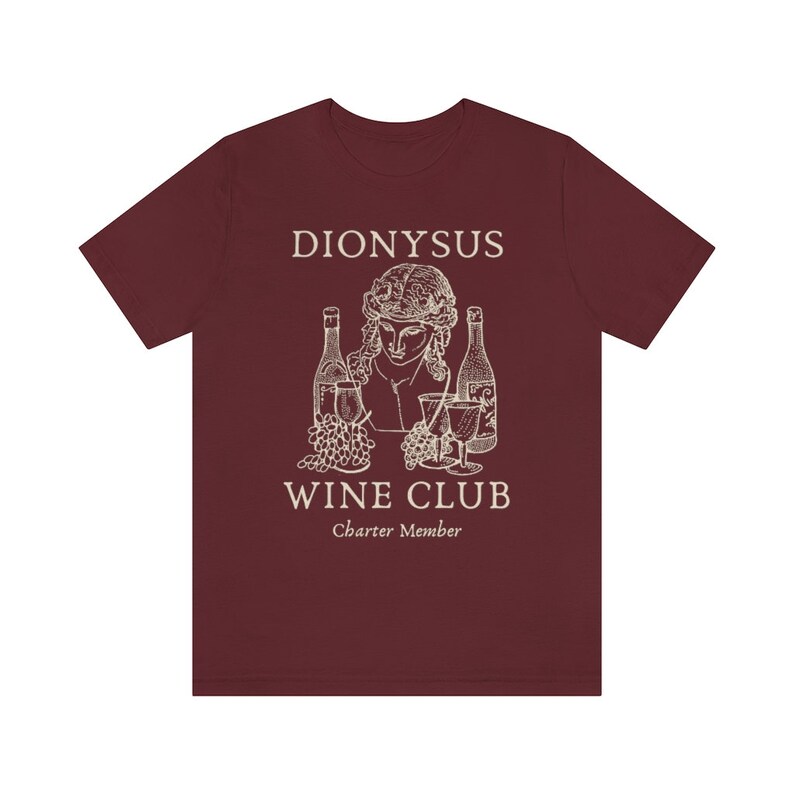 May include: A maroon t-shirt with a white graphic of a bust of Dionysus, the Greek god of wine, with grapes and bottles of wine. The text "Dionysus Wine Club Charter Member" is printed below the graphic.