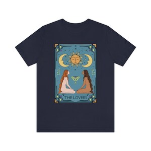 May include: Navy blue t-shirt with a vintage tarot card design featuring two figures, a sun, and a moon. The card reads "THE LOVERS".