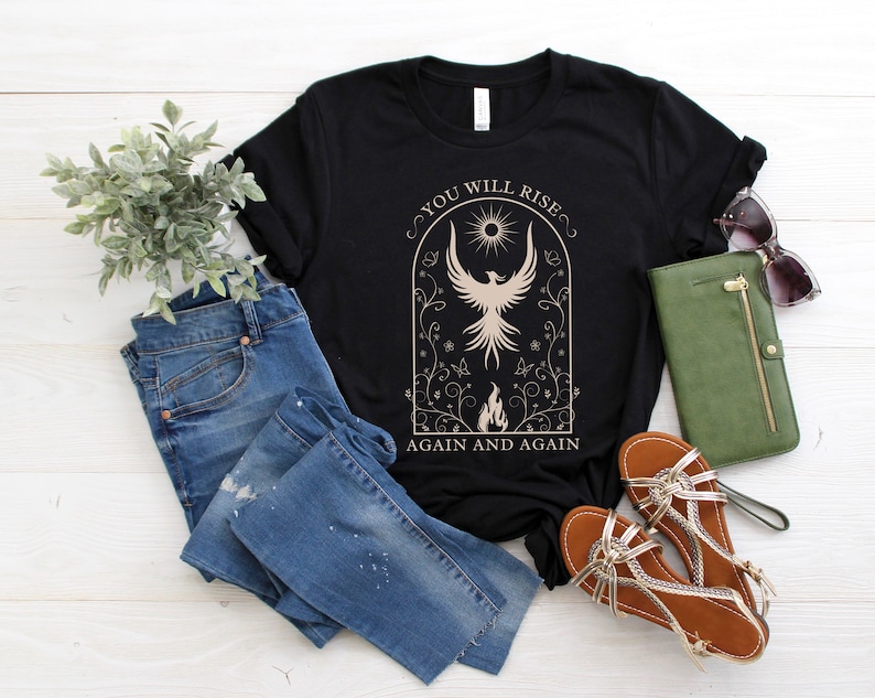 May include: Black t-shirt with a graphic of a phoenix rising from flames in a circle with the text "You Will Rise Again and Again".