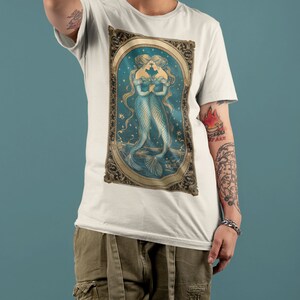 Puede incluir: Camiseta blanca con una ilustraci&oacute;n vintage de dos sirenas con las colas entrelazadas, enmarcada en oro sobre un fondo azul y dorado.
