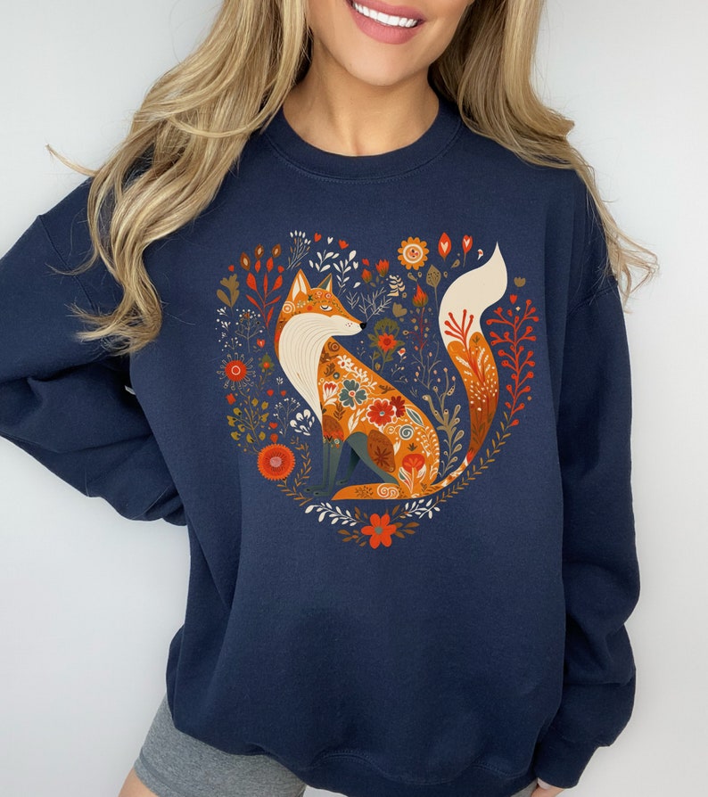 May include: A navy blue sweatshirt featuring a graphic of a fox surrounded by flowers in a heart shape. The fox is orange and white with floral details.