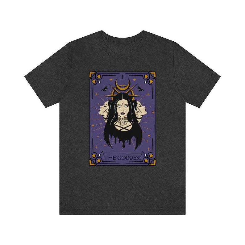 May include: A dark grey t-shirt with a purple and gold tarot card design. The card depicts a woman with three faces and the text "THE GODDESS".