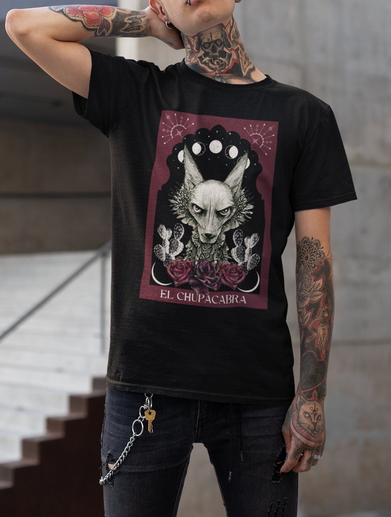 May include: Black t-shirt with a graphic print of a creature with a red background. The graphic features a creature with a wolf-like head, a cactus, and the text "EL CHUPACABRA".