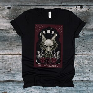May include: Black t-shirt with a graphic print of a wolf-like creature with red roses and the text "EL CHUPACABRA".