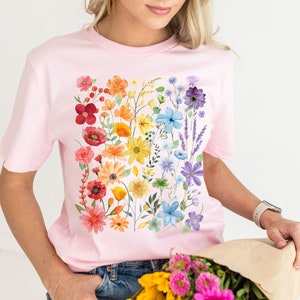 Puede incluir: Una camiseta rosa con estampado floral arco&iacute;ris. Las flores son de estilo acuarela y est&aacute;n dispuestas en una l&iacute;nea vertical.