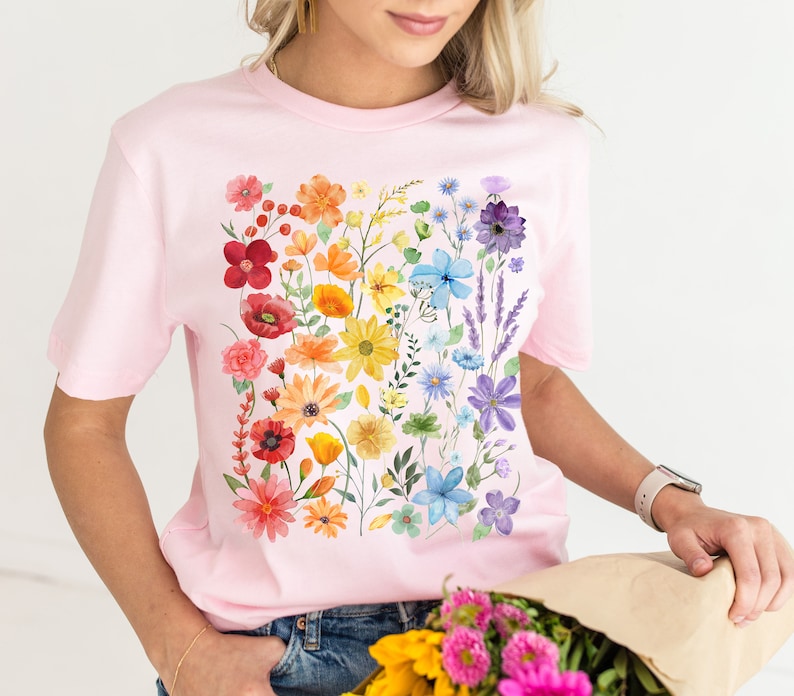 Puede incluir: Una camiseta rosa con estampado floral arco&iacute;ris. Las flores son de estilo acuarela y est&aacute;n dispuestas en una l&iacute;nea vertical.