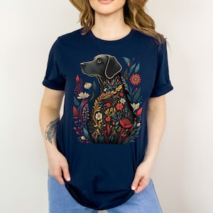 May include: A navy blue t-shirt with a black dog silhouette surrounded by colorful flowers. The dog is looking to the left and the flowers are in shades of red, yellow, orange, and green.