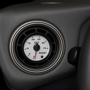 May include: Close-up of a car dashboard featuring a boost gauge. The gauge has a white face with black markings and a red needle. The text "EFT" and "BOOST" are visible. The gauge is set in a gray panel with a silver trim, next to a black steering wheel.