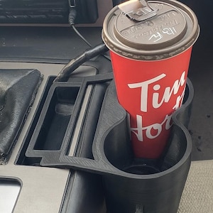 May include: Black 3D-printed car cup holder with a red Tim Hortons coffee cup. The cup holder is designed to fit in a car's center console. The coffee cup has a brown lid and white text.