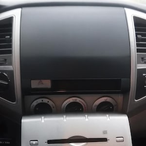 May include: Silver car stereo system with a CD player, AM/FM radio, and various control buttons. The dashboard is black and gray, with air vents and climate control knobs. The gear shift is visible.