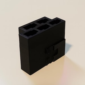 May include: A black, rectangular plastic component with multiple rectangular openings on top and a unique interlocking design on the side. The object is likely an electrical connector or housing for electronic components.