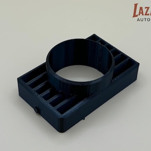 May include: A dark blue, 3D-printed automotive part. The part consists of a rectangular base with a series of vertical slots and a circular ring on top. The Lazarus Auto Parts logo is in the upper right corner.