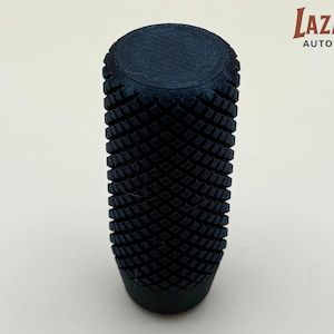 May include: A black, cylindrical auto part with a textured, diamond-patterned surface. The top is flat and also textured. The product is a replacement part for vehicles.