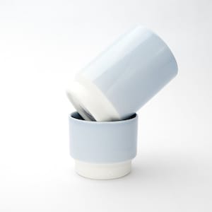 May include: Two light blue ceramic mugs with white rims. The mugs are stacked on top of each other.