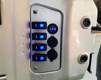Könnte beinhalten: Eine silberne Platte mit vier blau beleuchteten Schaltern, einer digitalen Spannungsanzeige mit 12,3 Volt und zwei Gleichstromsteckdosen. Die Platte ist auf einer größeren silbernen Oberfläche montiert.