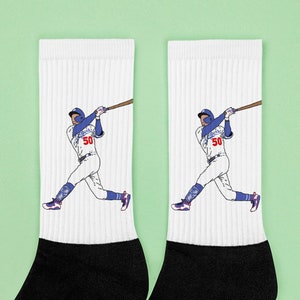 May include: A pair of white crew socks with a black baseball player illustration wearing a blue and white uniform with the number 50 on the front. The socks have black heels and toes.