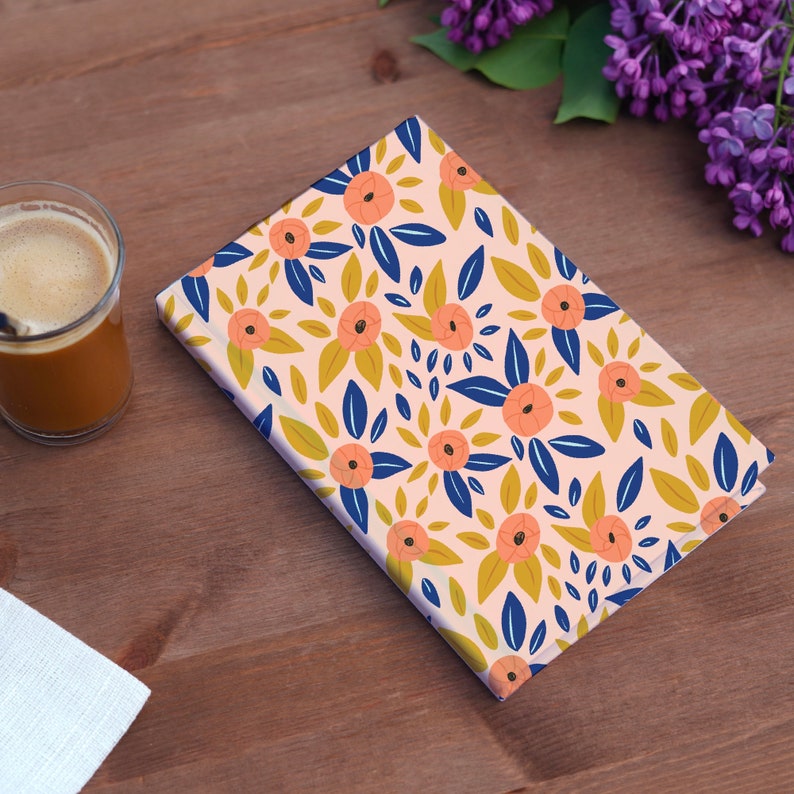 Pode incluir: Um caderno rosa com um padr&atilde;o floral com flores de p&ecirc;ssego, folhas azuis e detalhes amarelos.
