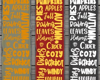 May include: Three rectangular wooden signs with autumn-themed text. The signs are in olive green, red, and black. The text includes words like "Pumpkins," "Apples," "Fall," "Harvest," and "Cider" in orange and white fonts. The signs have a distressed look.