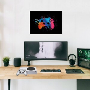 K&ouml;nnte beinhalten: Abstrakte Malerei eines Videospiel-Controllers in leuchtenden Farben auf schwarzem Hintergrund. Der Controller ist in Blau, Orange und Pink dargestellt. Eine Spielkonsole, ein Controller und ein Computer-Setup befinden sich auf einem Holztisch.