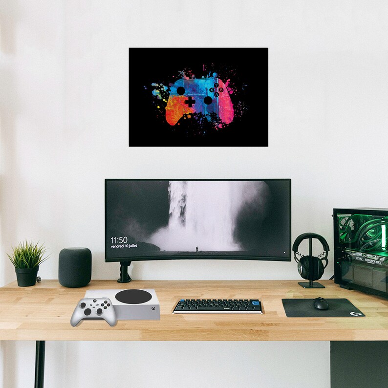 K&ouml;nnte beinhalten: Abstrakte Malerei eines Videospiel-Controllers in leuchtenden Farben auf schwarzem Hintergrund. Der Controller ist in Blau, Orange und Pink dargestellt. Eine Spielkonsole, ein Controller und ein Computer-Setup befinden sich auf einem Holztisch.