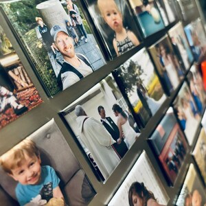 May include: A collage of framed photographs on a silver surface. The photos feature a variety of subjects, including people, landscapes, and indoor scenes. Some of the photos are in color, while others are in black and white.