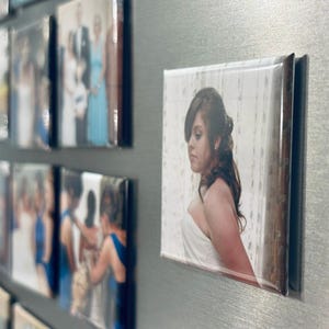 May include: A close-up of a photo magnet featuring a woman in a white dress. The photo is on a silver background with other magnets.