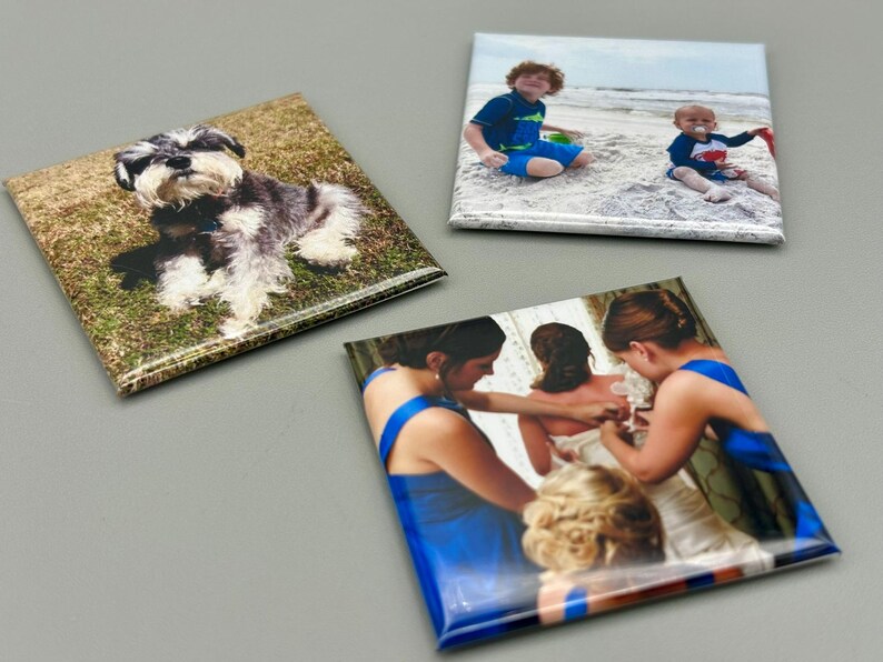May include: Three square photo magnets with different images. The first magnet features a small black and gray dog sitting on green grass. The second magnet shows two children on a beach. The third magnet shows three people in blue dresses getting ready for a wedding.