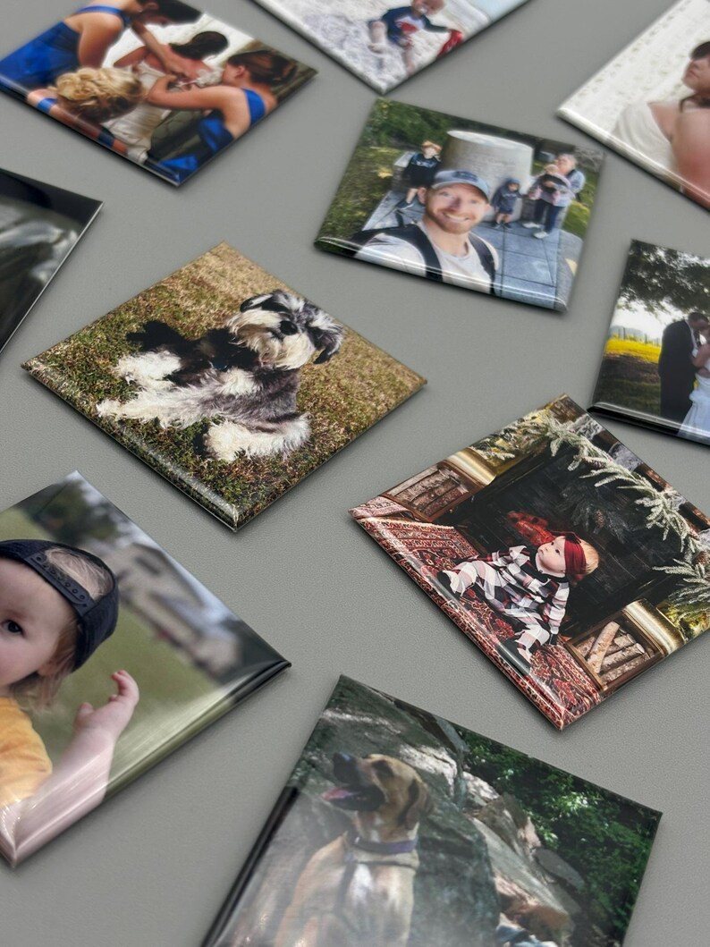 May include: A collection of square photo magnets with various images, including a family portrait, a dog, a baby, and a couple. The magnets are arranged on a gray surface.