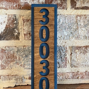 May include: A wooden sign with the number 30030 painted in black on it. The sign has a dark blue border and is standing on a wooden surface.