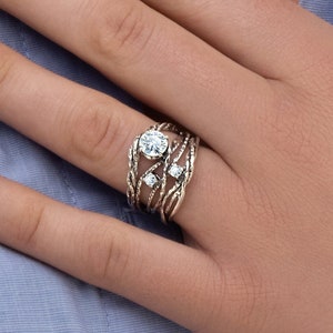 May include: A silver ring with multiple bands and clear gemstones. The ring is worn on a person's finger.