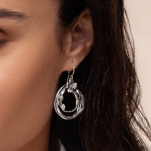 May include: Silver hoop earrings with a delicate floral design and a small butterfly charm.