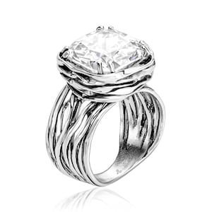 May include: A silver ring with a large, clear, square-shaped gemstone set in a twisted, branch-like design. The ring has a textured band.
