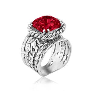 May include: A sterling silver ring featuring a large, square-cut, vibrant red gemstone. The ring has a detailed, nature-inspired design with leaves and a rope-like texture around the gemstone setting. The band is wide and intricately carved.