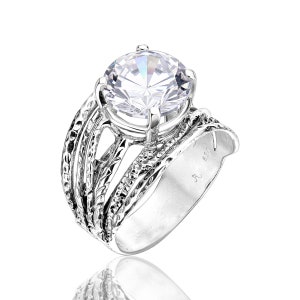 May include: A silver ring with a large, clear, round gemstone set in a textured band. The band is made of multiple strands of silver wire that are twisted and woven together.