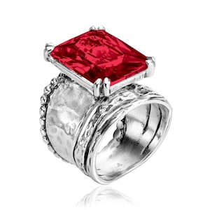 May include: A silver ring featuring a large, rectangular, vibrant red gemstone. The ring has a textured band with a hammered effect and a beaded edge. The gemstone is set in a silver bezel.