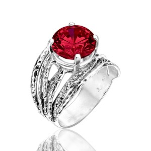 May include: A silver ring with a large, round, faceted, red gemstone. The ring has a textured band with multiple layers and a polished finish. The gemstone is held by four prongs.