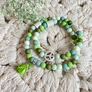May include: Two layered bracelets with green and white beads, a peace sign charm, and a green tassel.