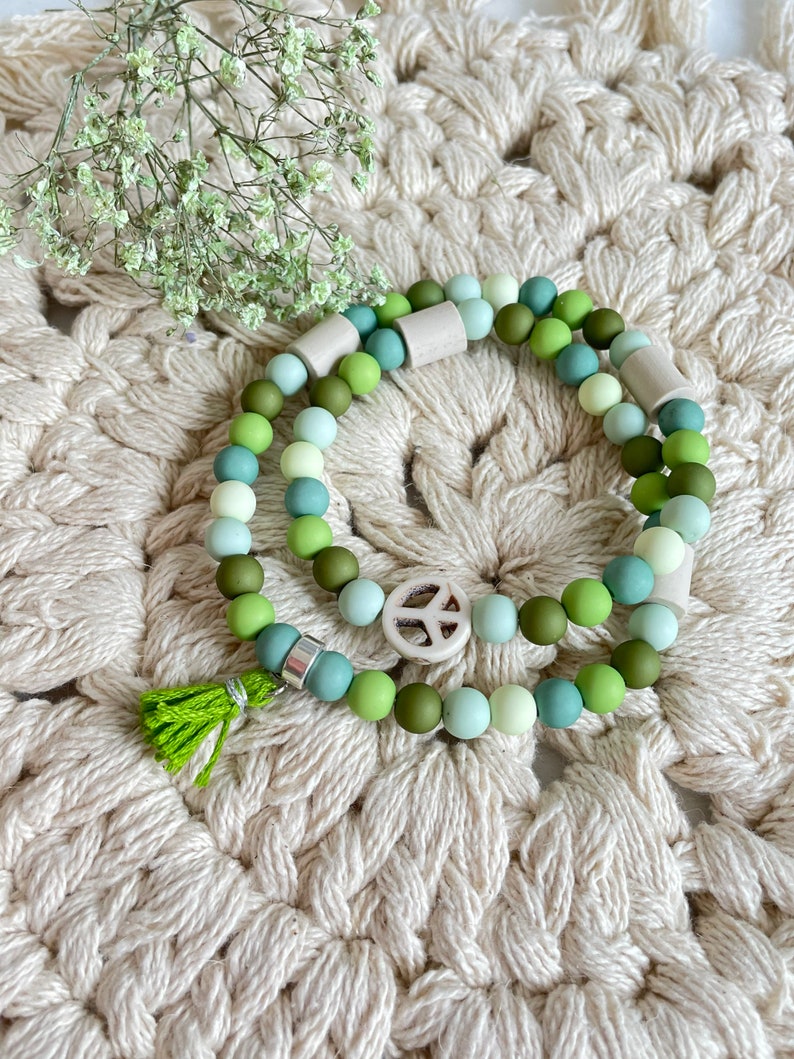 May include: Two layered bracelets with green and white beads, a peace sign charm, and a green tassel.