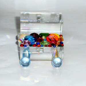 May include: A clear acrylic treasure chest filled with colorful jewels and beads. The chest has two round clear acrylic knobs on the front.