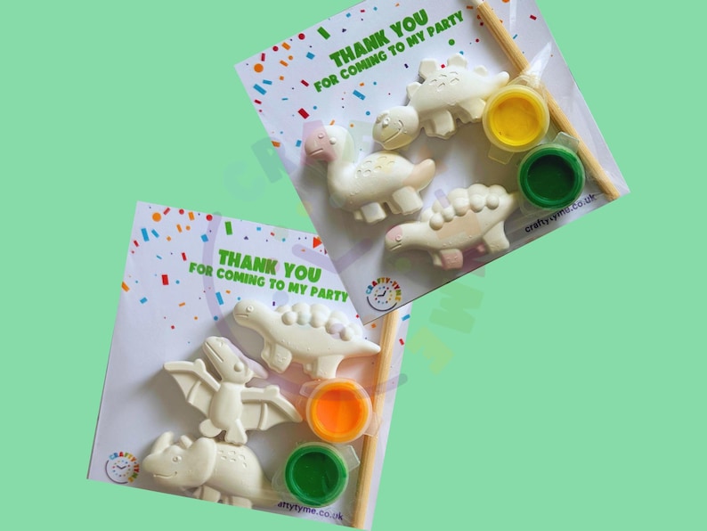 Peut inclure: Kits de bricolage &agrave; peindre soi-m&ecirc;me sur le th&egrave;me des dinosaures. Chaque kit comprend plusieurs figurines de dinosaures, des pots de peinture jaune, orange et vert, et un pinceau. L'emballage contient le texte "THANK YOU FOR COMING TO MY PARTY" avec des confettis color&eacute;s.