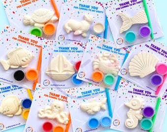 May include: A collection of ten individual party favor kits, each featuring a white plaster figurine of a sea creature or boat, two small paint pots, and a paintbrush, all packaged on a card with the text Thank You For Coming To My Party.
