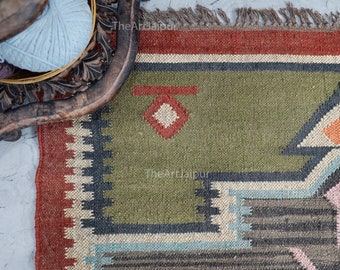 May include: A green, red and black patterned rug with fringe. The rug has a geometric design with a diamond shape in the centre.